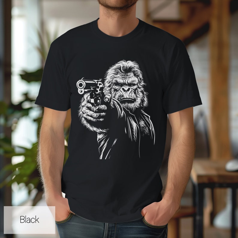 以下が含まれることがあります： 銃を持ったゴリラの白いグラフィックがプリントされた黒いTシャツ
