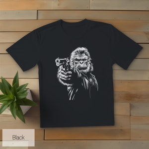 以下が含まれることがあります： 銃を持ったゴリラの白いグラフィックがプリントされた黒いTシャツ