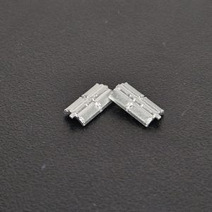 Puede incluir: Dos pequeños componentes metálicos rectangulares de tono plateado con una serie de crestas paralelas en relieve y una línea horizontal central. Cada pieza tiene un perfil ligeramente curvado y pequeñas pestañas en los extremos.