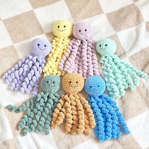 May include: A collection of seven crocheted octopus toys in various pastel and bright colors including yellow, lavender, mint green, sage green, gold, and blue. Each octopus features a round head, black bead eyes, a stitched smile, and curly tentacles.