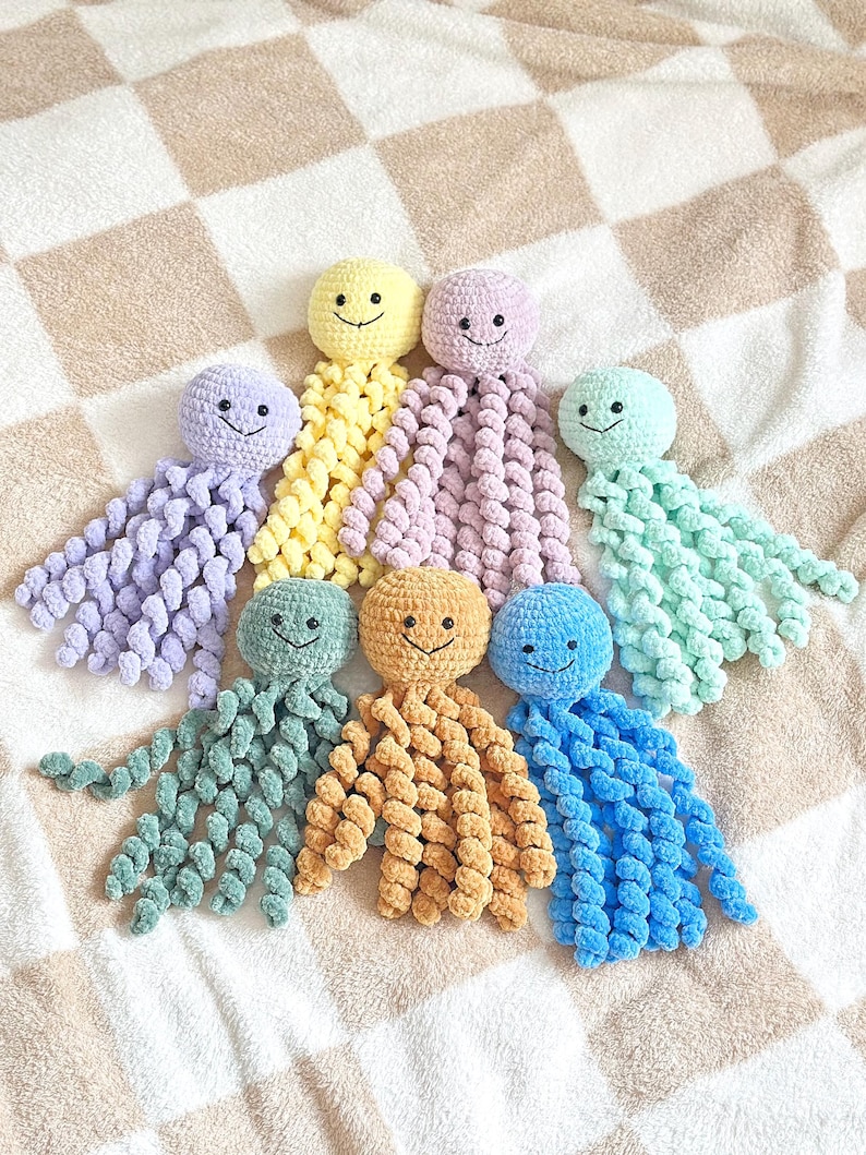 May include: A collection of seven crocheted octopus toys in various pastel and bright colors including yellow, lavender, mint green, sage green, gold, and blue. Each octopus features a round head, black bead eyes, a stitched smile, and curly tentacles.