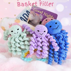 May include: A collection of three crocheted octopus toys in mint green, lavender, and blue, each with curly tentacles and embroidered faces. Behind them are a patterned swaddle blanket and a children's book titled Good Night, with text above.