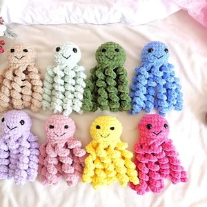 May include: Eight small, handmade crochet octopus plush toys arranged in two rows. Each octopus features a round head, black safety eyes, a stitched smile, and eight curly, spiraled tentacles made from soft, plush yarn in various solid colors.