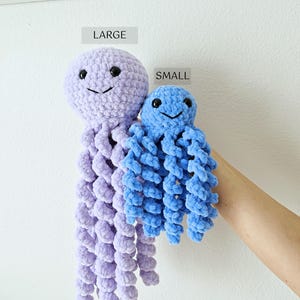 May include: Two crochet jellyfish toys made of soft yarn. The larger jellyfish is light purple, and the smaller jellyfish is bright blue. Both have round heads, black plastic safety eyes, stitched smiles, and multiple long, spiraling tentacles.