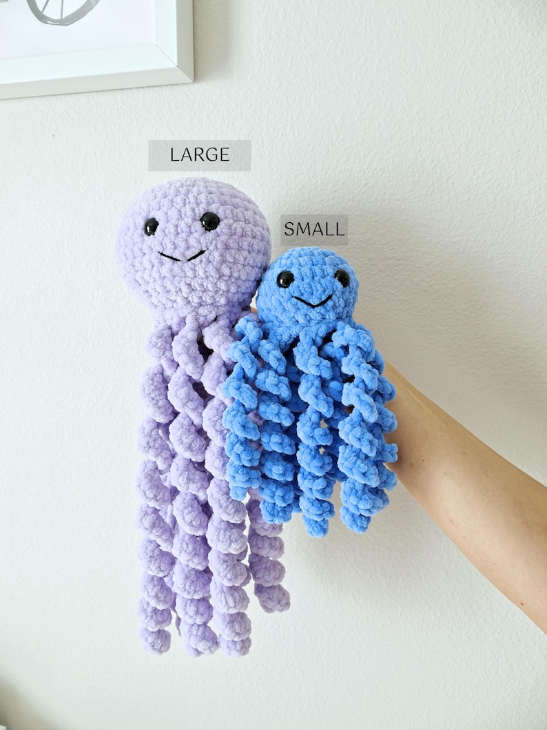 May include: Two crochet jellyfish toys made of soft yarn. The larger jellyfish is light purple, and the smaller jellyfish is bright blue. Both have round heads, black plastic safety eyes, stitched smiles, and multiple long, spiraling tentacles.