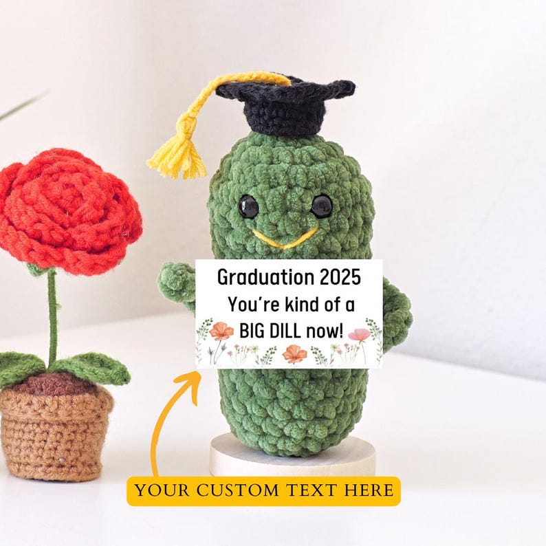 A green pickle in a graduation cap holding a white sign with black text