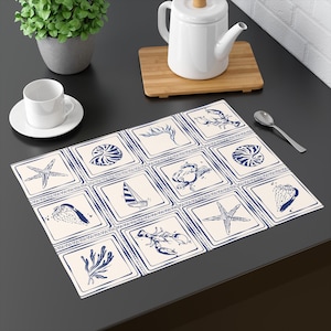May include: A rectangular placemat with a nautical theme. The placemat features a grid of cream-colored squares, each containing a blue illustration of marine life, including starfish, seashells, and a sailboat. The placemat is on a dark surface.