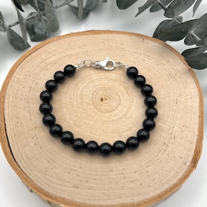 May include: A black beaded bracelet with a silver clasp. The bracelet is on a wooden surface.