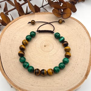 May include: A brown and green beaded bracelet with a brown cord closure. The beads are made of tiger's eye and malachite.