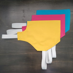 May include: Three fabric neck gaiters in yellow, pink, and blue colors. The yellow gaiter has white straps attached to it.