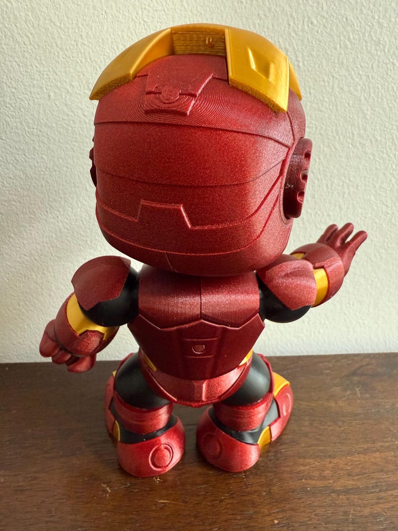 Peut inclure: figurine Iron Man rouge et or avec une surface textur&eacute;e. La figurine est debout, les bras tendus, et fait face &agrave; l'arri&egrave;re de la cam&eacute;ra.