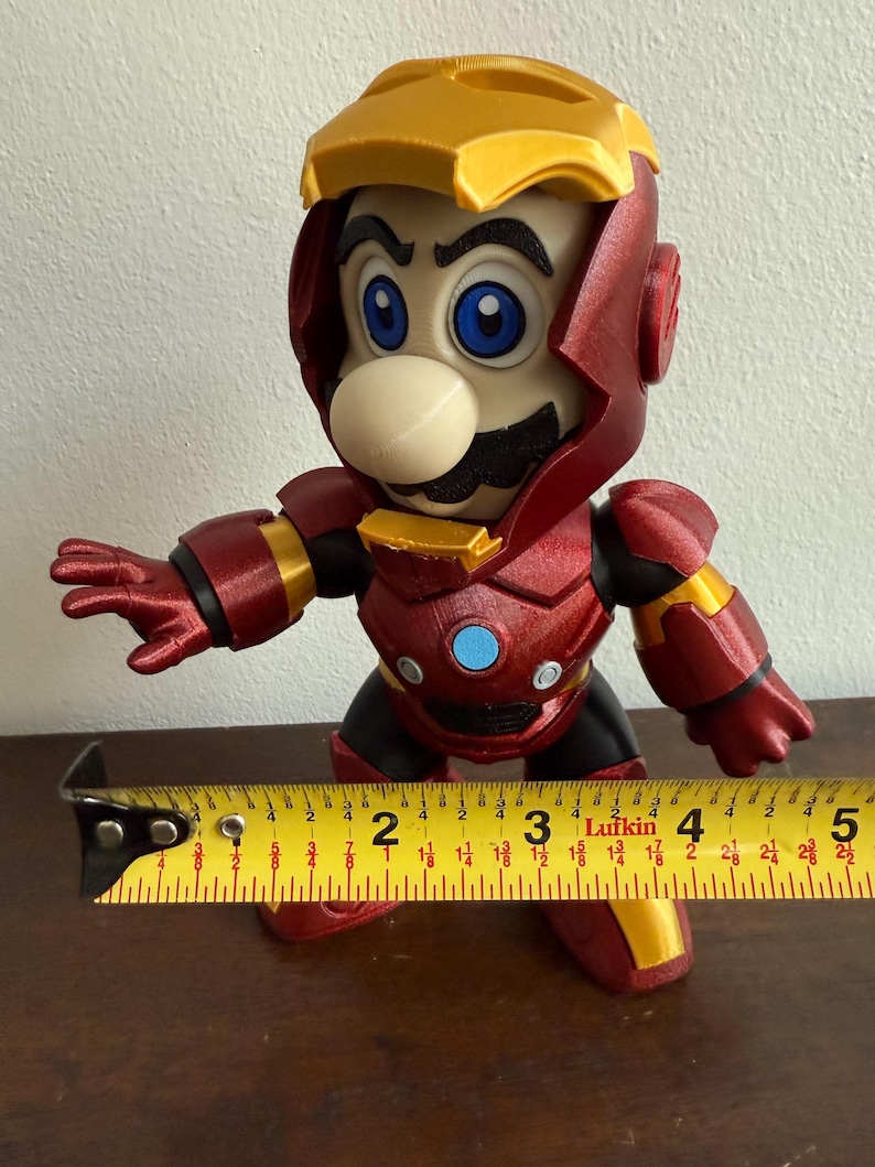 Peut inclure: Une figurine rouge et or d'un personnage portant une armure d'Iron Man. Le personnage a une moustache et un grand nez. La figurine mesure environ 18 cm de haut.