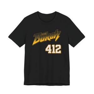 Peut inclure: T-shirt noir avec le mot "Burgh" en jaune et noir, et le numéro "412" en blanc avec un contour jaune. Le t-shirt est de style col rond.