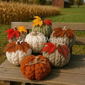 May include: A collection of handmade, textured pumpkins in various colors, including orange, white, and green, adorned with faux fall leaves. The pumpkins are arranged on a wooden bench, with a rural backdrop.