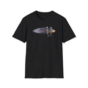 May include: Black t-shirt featuring a colorful surfboard design with two gray alien figures standing next to it. The surfboard has a vibrant, multicolored pattern. The t-shirt is made of a soft material.