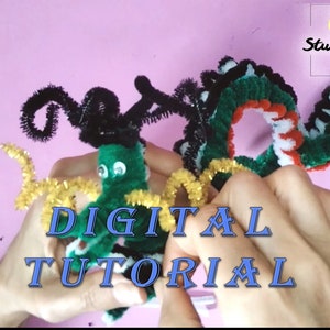 Puede incluir: Dos dragones verdes de limpiapipas, uno con rayas blancas y negras y el otro con cuernos negros, est&aacute;n siendo sostenidos por manos. El texto "DIGITAL TUTORIAL" est&aacute; en letras azules sobre un fondo rosa.