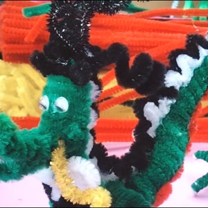 Puede incluir: Un drag&oacute;n de limpiapipas verde, negro, blanco y rojo con ojos saltones. El drag&oacute;n est&aacute; enroscado y tiene una cola de limpiapipas dorada.