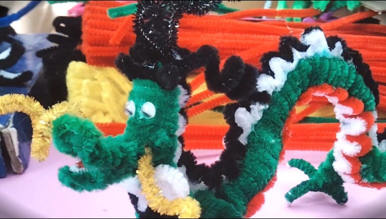 Puede incluir: Un drag&oacute;n de limpiapipas verde, negro, blanco y rojo con ojos saltones. El drag&oacute;n est&aacute; enroscado y tiene una cola de limpiapipas dorada.