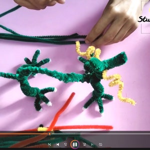 Puede incluir: Un proyecto de artesan&iacute;a de drag&oacute;n de limpiapipas verde en progreso. El drag&oacute;n est&aacute; hecho con limpiapipas verdes y tiene una cola de limpiapipas amarilla. El drag&oacute;n est&aacute; sobre una superficie rosa. El texto "Art Studio Shevchenko" es visible en la esquina superior derecha de la imagen.