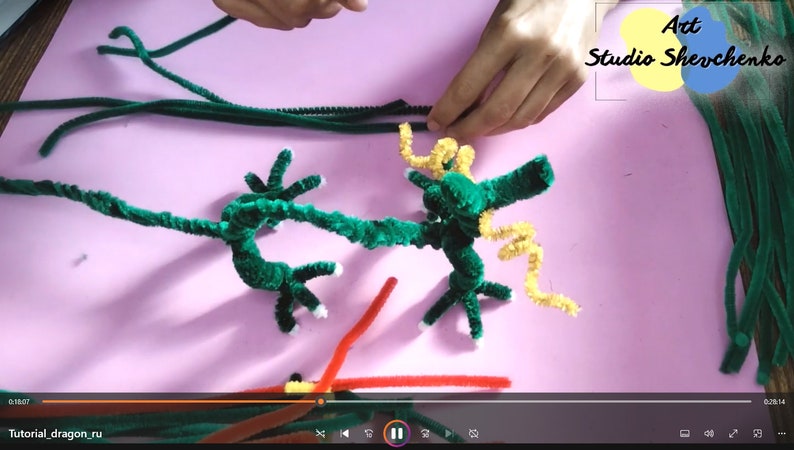 Puede incluir: Un proyecto de artesan&iacute;a de drag&oacute;n de limpiapipas verde en progreso. El drag&oacute;n est&aacute; hecho con limpiapipas verdes y tiene una cola de limpiapipas amarilla. El drag&oacute;n est&aacute; sobre una superficie rosa. El texto "Art Studio Shevchenko" es visible en la esquina superior derecha de la imagen.