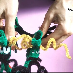 Puede incluir: Dos ara&ntilde;as de limpiapipas verdes con patas negras y ojos saltones. Las ara&ntilde;as est&aacute;n conectadas por un limpiapipas amarillo. El texto "Art Studio Shevchenko" es visible en el fondo.