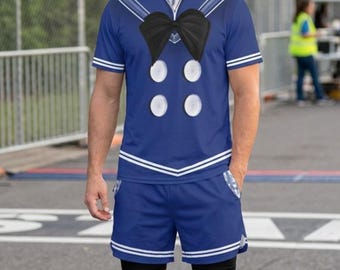 May include: A blue sailor-themed t-shirt and matching shorts set featuring a black bow tie graphic, white circular buttons, and white trim. The outfit is paired with a wide-brimmed straw sombrero with a dark brown and gold patterned band.
