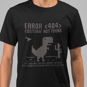 Puede incluir: Una camiseta negra con un gráfico de dinosaurio pixelado gris y el texto "ERROR <404> COSTUME NOT FOUND". El texto debajo del dinosaurio dice "THE COSTUME YOU ARE LOOKING FOR WAS LOST REMOVED OR MIGHT HAVE NEVER EXISTED."