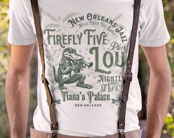 May include: A white t-shirt with a green graphic of an alligator playing a trumpet. The graphic includes the text "New Orleans Jazz", "Music from the Bayou", "Firefly Five", "Plus Lou", "Nightly at 7PM", and "Tiana's Palace, New Orleans".