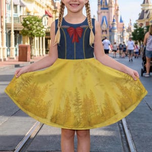 Puede incluir: Un vestido amarillo y azul sin mangas con un estampado de bosque en la falda y un lazo rojo. El vestido está diseñado para parecerse a un disfraz de princesa. El vestido lo lleva una persona.