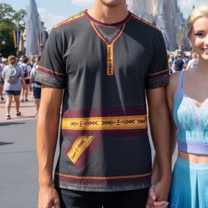 May include: Dark gray t-shirt with a burgundy and gold geometric pattern. The short-sleeved shirt has a crew neck and a decorative design down the front. The shirt is part of a themed collection.