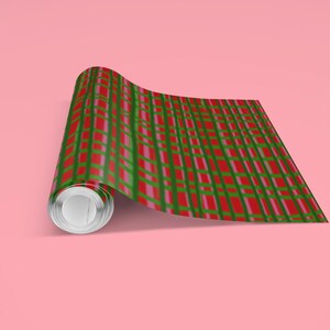 May include: A roll of wrapping paper with a red, green, and pink plaid pattern. The paper is partially unrolled, revealing the pattern. The background is a solid pink color.