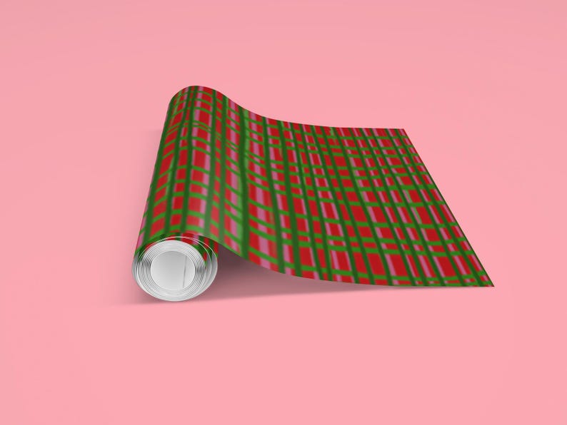 May include: A roll of wrapping paper with a red, green, and pink plaid pattern. The paper is partially unrolled, revealing the pattern. The background is a solid pink color.