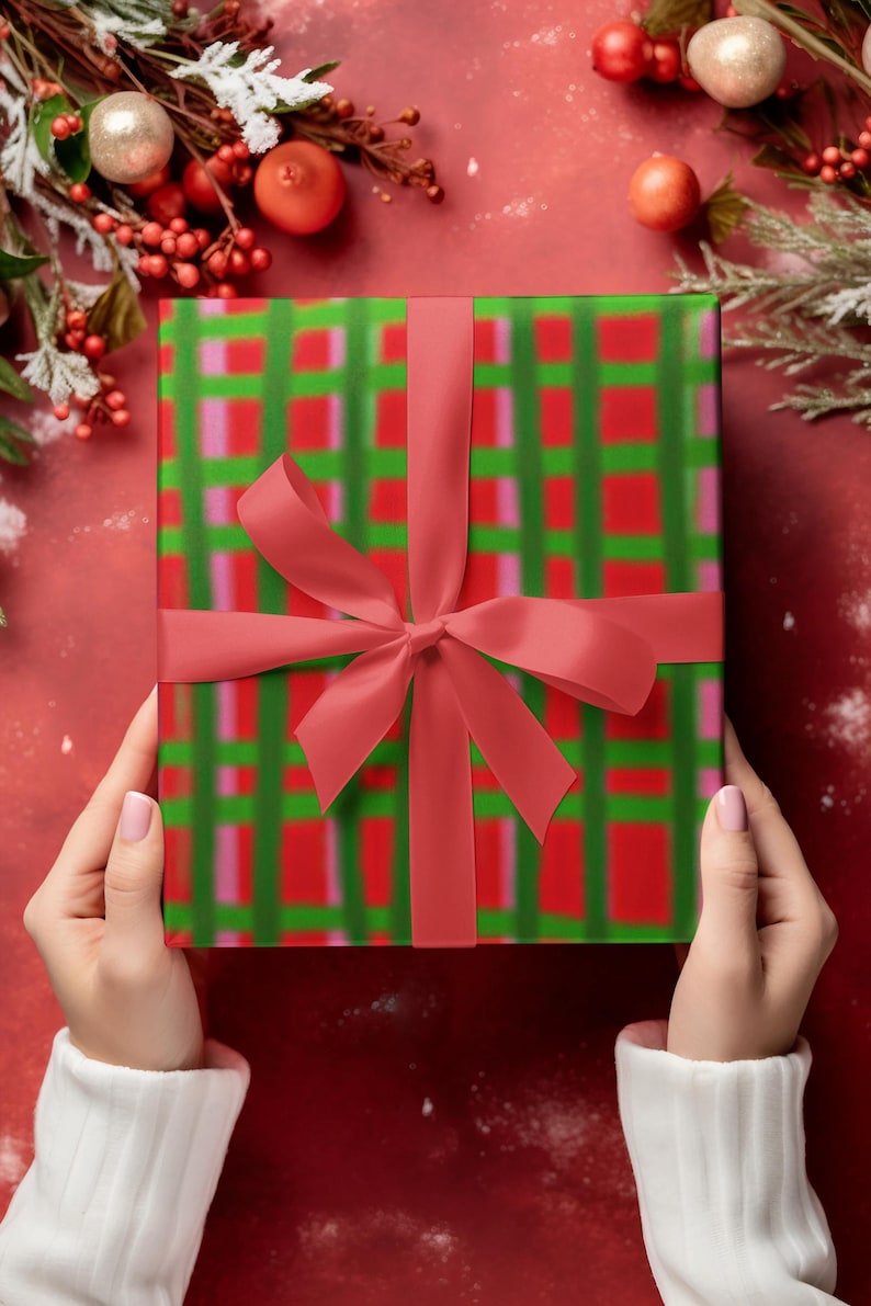 May include: A wrapped gift with a red ribbon and bow. The wrapping paper has a green and red plaid pattern. The gift is held by hands wearing a white sweater, set against a red background with Christmas decorations.