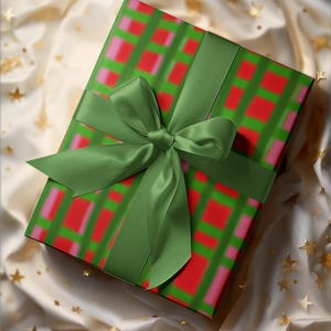 May include: A wrapped gift box with a green ribbon and bow. The wrapping paper has a green grid pattern with red and pink squares. The gift is on a cream-colored fabric with gold star accents.