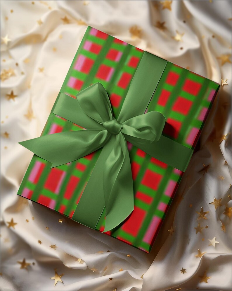 May include: A wrapped gift box with a green ribbon and bow. The wrapping paper has a green grid pattern with red and pink squares. The gift is on a cream-colored fabric with gold star accents.