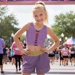 May include: A young girl in a purple crop top and shorts set. The top has a lace-up design and the shorts have a gold waistband and decorative trim. The outfit is worn during a race.
