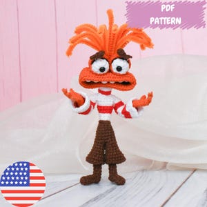 Puede incluir: Patrón de crochet para un personaje rojo y marrón con una camisa a rayas blancas y rojas. El personaje tiene una cabeza grande con ojos grandes y una boca ancha. El patrón está disponible para descargar en PDF.