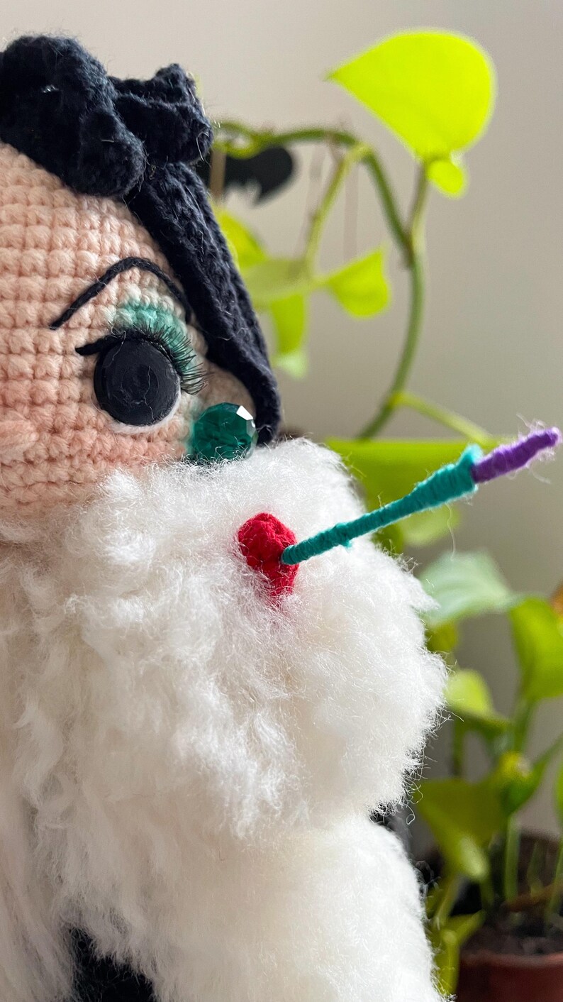Puede incluir: Una mu&ntilde;eca de crochet con cabello negro, ojos verdes y barba blanca. La mu&ntilde;eca lleva un vestido negro y tiene una nariz roja.