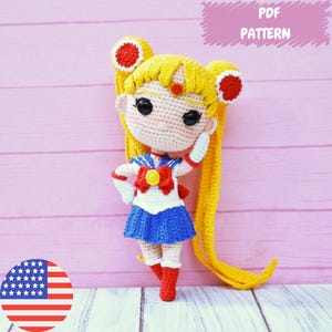 Puede incluir: Patrón de crochet para una muñeca amigurumi de Sailor Moon. La muñeca lleva un uniforme de marinero azul y blanco con un lazo rojo y una estrella amarilla. La muñeca tiene el pelo largo amarillo y una diadema roja. El patrón está disponible para descargar en PDF.