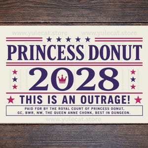 May include: A rectangular sign with a cream background featuring dark blue text that reads PRINCESS DONUT 2028, THIS IS AN OUTRAGE!, and smaller text below. The design includes red and blue stars, red horizontal lines, and a small red crown icon.