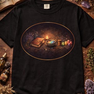 May include: Black t-shirt featuring an oval design with a mystical theme. The design includes a lit candle, a book, a bowl with colorful contents, and spools of thread. The shirt is made of a soft material.
