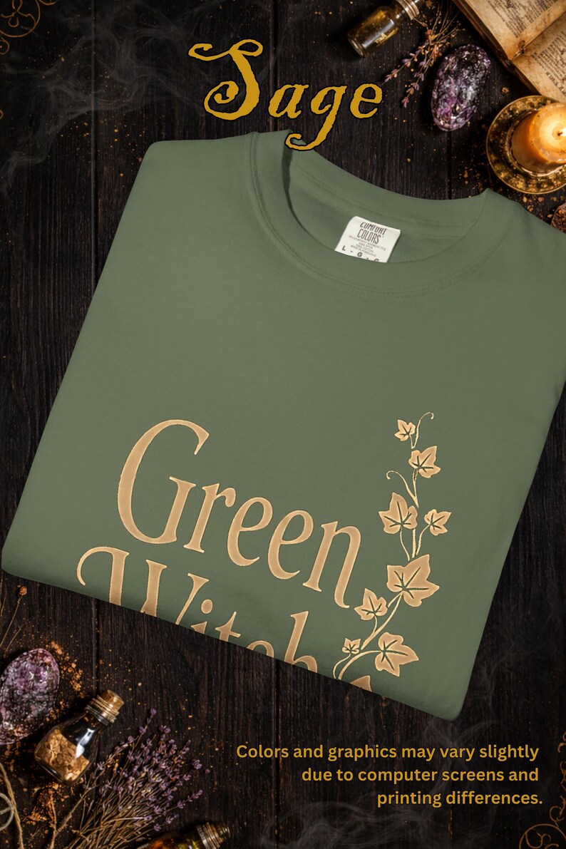 Peut inclure: T-shirt vert sauge avec l'inscription "Green Witch" en lettres dor&eacute;es, accompagn&eacute;e d'un motif de feuilles. Le t-shirt est en mati&egrave;re Comfort Colors. Le texte "Colors and graphics may vary slightly due to computer screens and printing differences" est &eacute;galement visible.