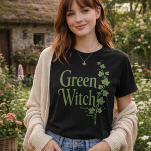 Peut inclure: Un t-shirt noir avec l'inscription "Green Witch" en vert et un motif de vigne verte. L'expression "Rooted in Nature" est en dessous. Le t-shirt est port&eacute; avec un cardigan cr&egrave;me et un jean bleu.