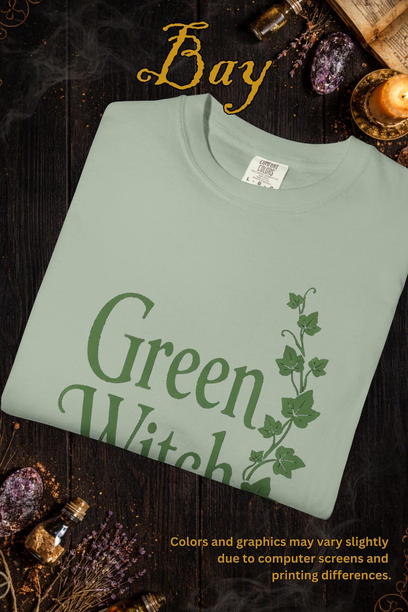 Peut inclure: T-shirt vert clair avec l'inscription "Green Witch" en vert fonc&eacute;, accompagn&eacute;e d'un motif de lierre vert. Le t-shirt est de la marque Comfort Colors. Le mot "Bay" est en haut. Le texte en bas indique que les couleurs peuvent varier.
