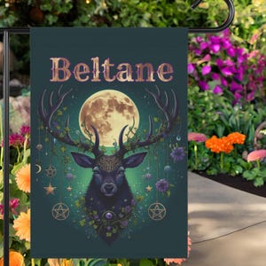 Puede incluir: Una bandera de jard&iacute;n verde con un fondo verde oscuro que presenta un ciervo negro con cuernos adornados con flores y enredaderas. El ciervo est&aacute; de pie frente a una luna llena y el texto "Beltane" est&aacute; escrito en letras doradas en la parte superior de la bandera.