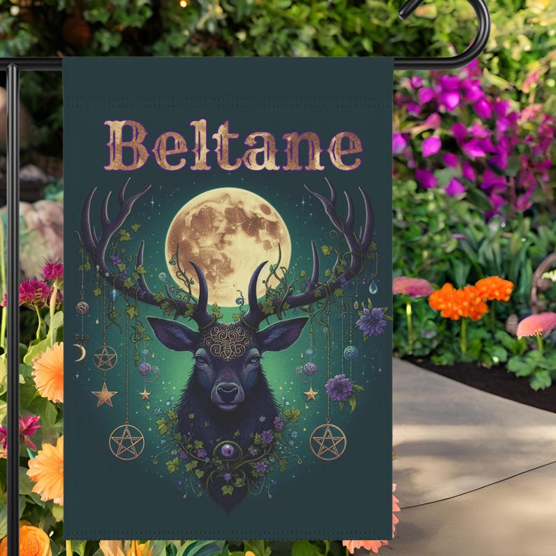 Puede incluir: Una bandera de jard&iacute;n verde con un fondo verde oscuro que presenta un ciervo negro con cuernos adornados con flores y enredaderas. El ciervo est&aacute; de pie frente a una luna llena y el texto "Beltane" est&aacute; escrito en letras doradas en la parte superior de la bandera.