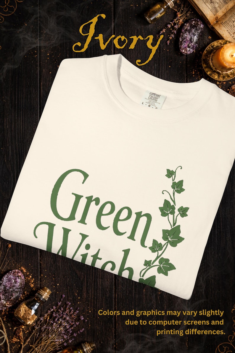 Peut inclure: T-shirt ivoire avec l'inscription "Green Witch" en vert et un motif de lierre vert. Le t-shirt est en mati&egrave;re douce. Le texte "Colors and graphics may vary slightly due to computer screens and printing differences" est &eacute;galement visible.