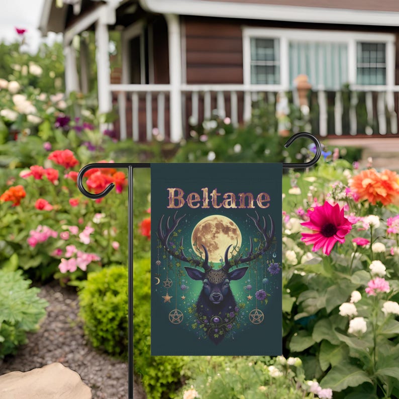 Puede incluir: Una bandera de jard&iacute;n verde con una silueta de ciervo negro, una luna llena y la palabra "Beltane" en letras doradas. El ciervo est&aacute; rodeado de flores y enredaderas.