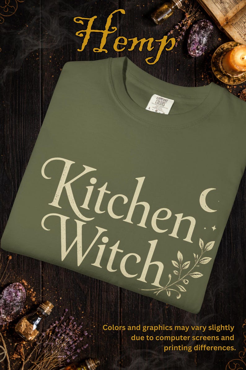 May include: Olive green t-shirt with the words "Kitchen Witch" in a vintage font, accented with a crescent moon and botanical illustration. The word "Hemp" is at the top. The shirt is made of Comfort Colors material.