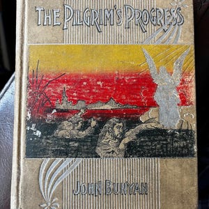 May include: A vintage book titled "The Pilgrim's Progress" by John Bunyan. The cover features a scene with two figures in the foreground and an angel in the background. The cover is a tan color with a gold and red design.